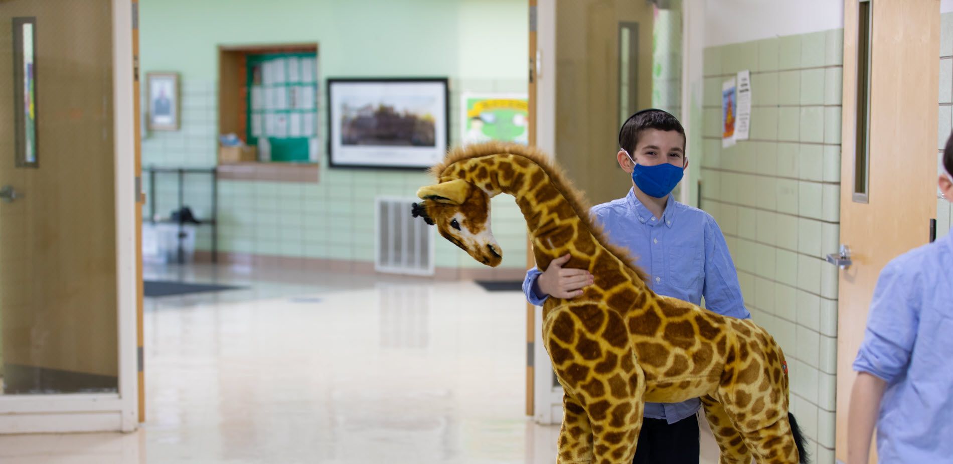 Young student carrying a stuffed giraffe toy into a classroom.